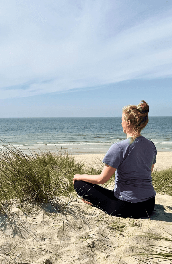 Frau beim Yoga in den Dünen - im Schneidersitz mit Blick auf das Meer